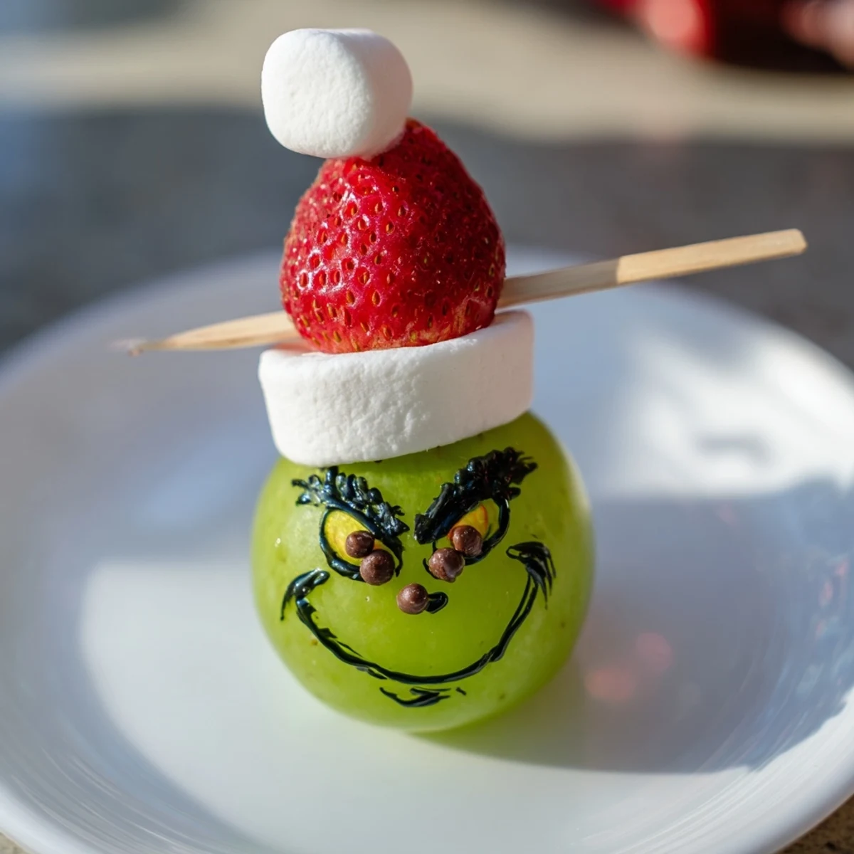 Green grape Grinch faces: A festive snack with a marshmallow Grinch head and strawberry hat.