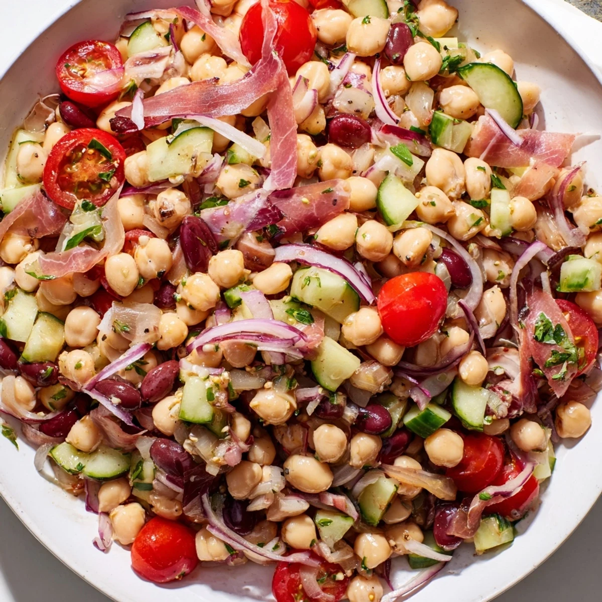 Vibrantly-colored dense bean salad with prosciutto, showcasing fresh herbs and crisp vegetables.