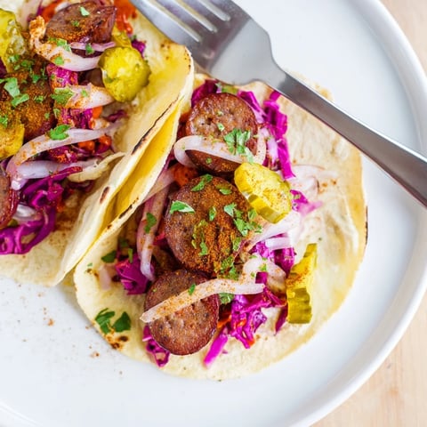 Smoky bratwurst in Berlin Currywurst Tacos, drizzled with curry ketchup and fresh, colorful toppings.