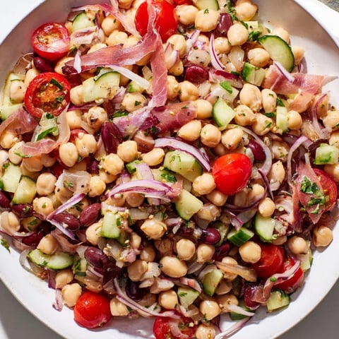 Vibrantly-colored dense bean salad with prosciutto, showcasing fresh herbs and crisp vegetables.